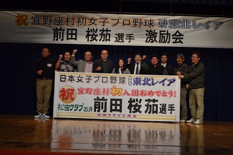 横断幕が掲げられおり、舞台の上で前田桜茄さんと関係者達9名が横に並んでいる写真